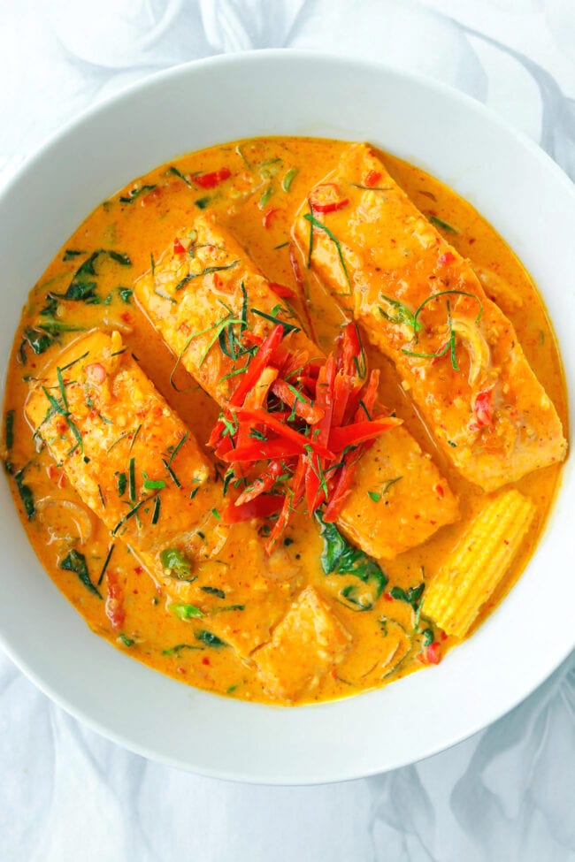 Top view of salmon fillets with choo chee red curry in a white round serving bowl.