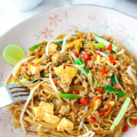 Front view of plate with fork tucked into stir-fried noodles dish. Text overlay "Pad Mee Korat" and "Pad Thai's Spicier Cousin!".