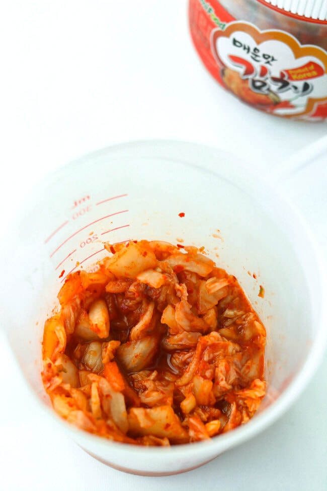 Kimchi in a measuring cup and kimchi jar in the back.