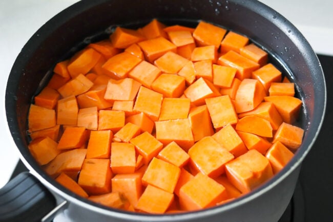 Cubed sweet potatoes in pot with water on stovetop.