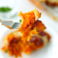 Fork holding up a bite of cheesy sweet potato mach with a piece of bacon. Text overlay "Spicy Loaded Sweet Potato Casserole" and "thatspicychick.com".