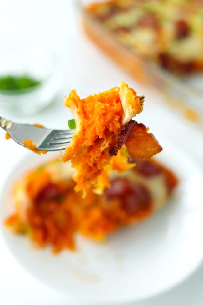 Fork holding up a bite of cheesy sweet potato mash and a piece of crispy bacon.