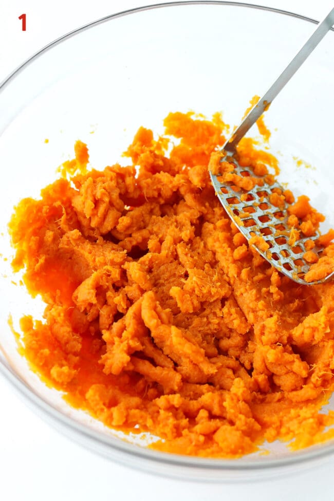 Sweet potato mash and a potato masher in a large mixing bowl.