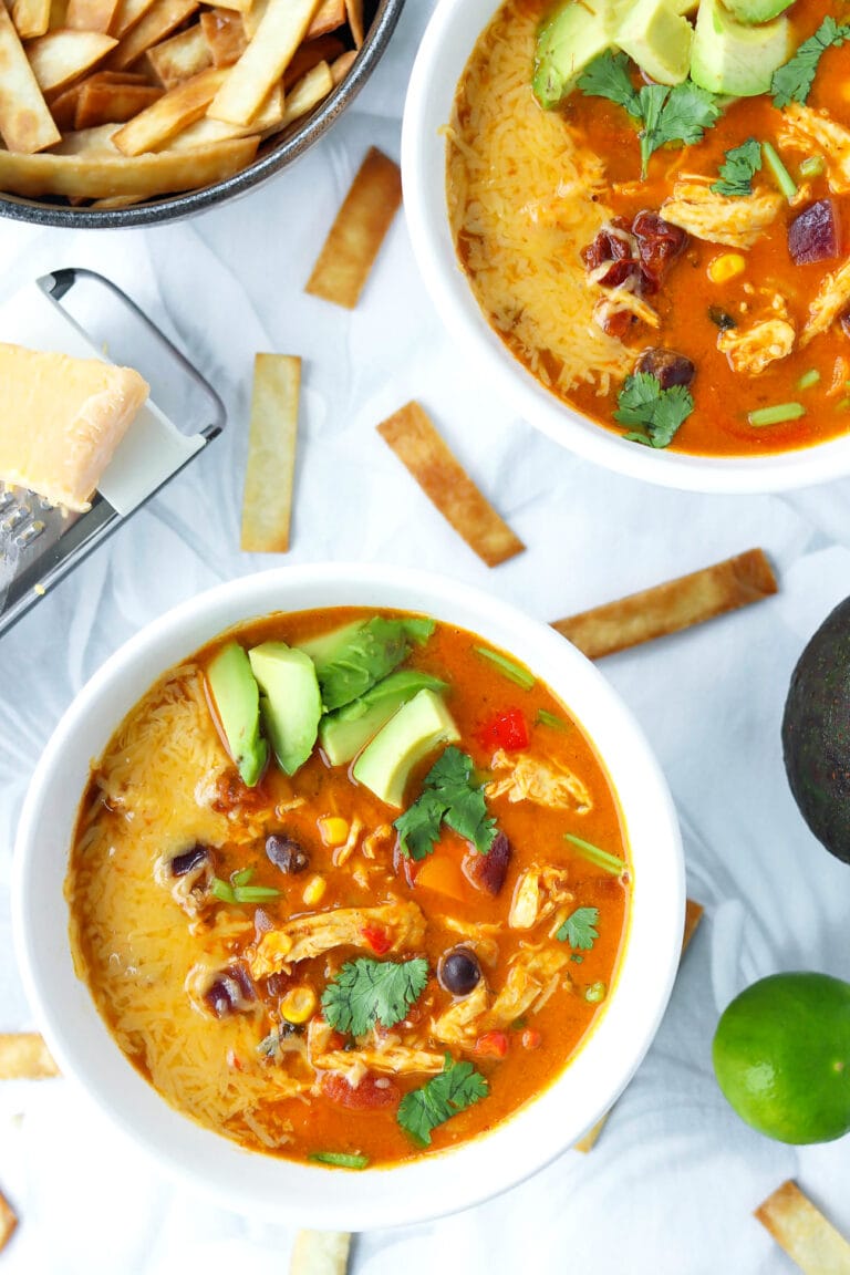Bowls with pumpkin chicken tortilla soup surrounded by toppings.
