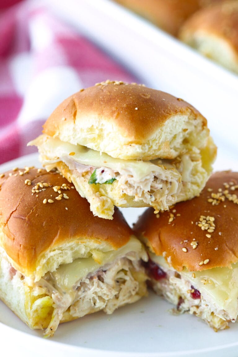 Three stacked turkey and chicken cranberry sliders on a plate.