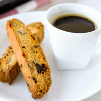 Close-up front view of two biscotti and a cup of coffee on a white plate.