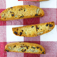Top view of five biscotti on a red and white checkered napkin. Text overlay "Cranberry Pecan Biscotti" and "thatspicychick.com".