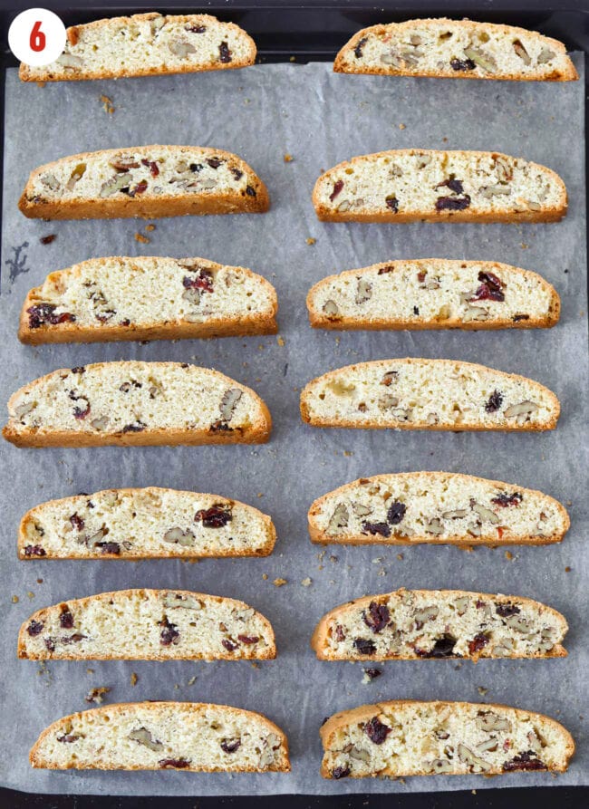 Biscotti pieces cut side down on a parchment paper lined baking tray.