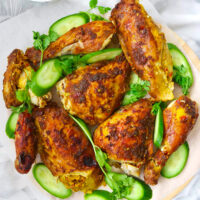 Cut chicken pieces, cucumber, and coriander on platter lined with baking paper. Text overlay "Spicy Thai Roast Chicken", "thatspicychick.com" and "with Spicy Dipping Sauce (Nam Jim Jaew)".