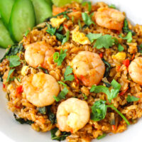 Front view of plate with spicy prawn fried rice with cucumber slices and a lime wedge.