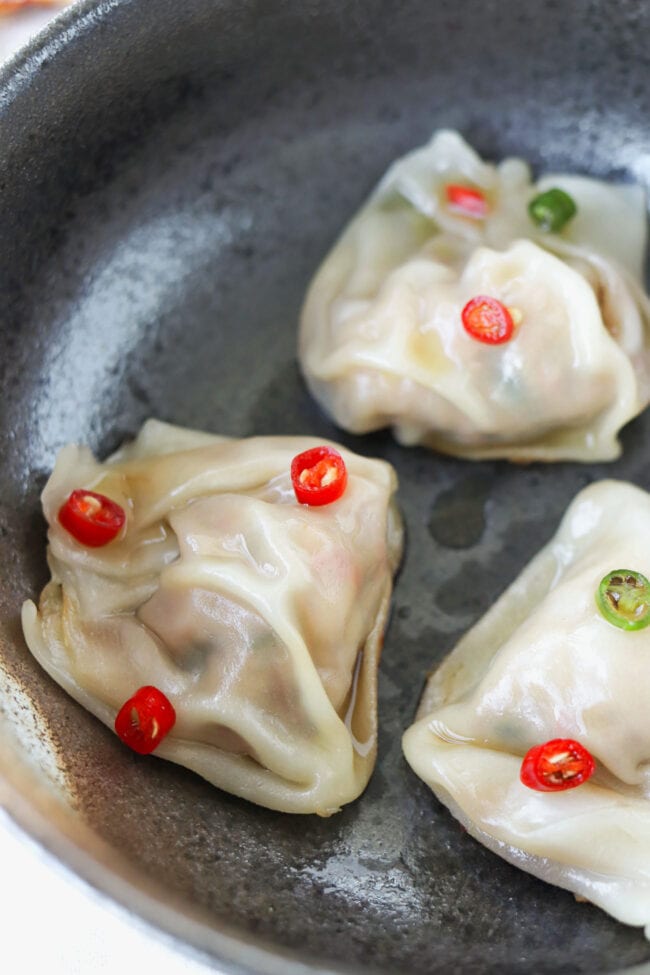 Close up of three spicy Thai basil wontons in a black bowl topped with fish sauce and chopped chilies.