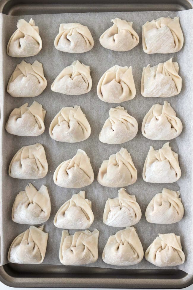 Assembled uncooked spicy Thai basil wontons lined up on a parchment paper lined tray.