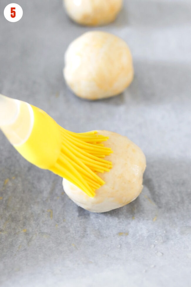 Brushing egg wash on a bagel ball with a yellow silicone brush.