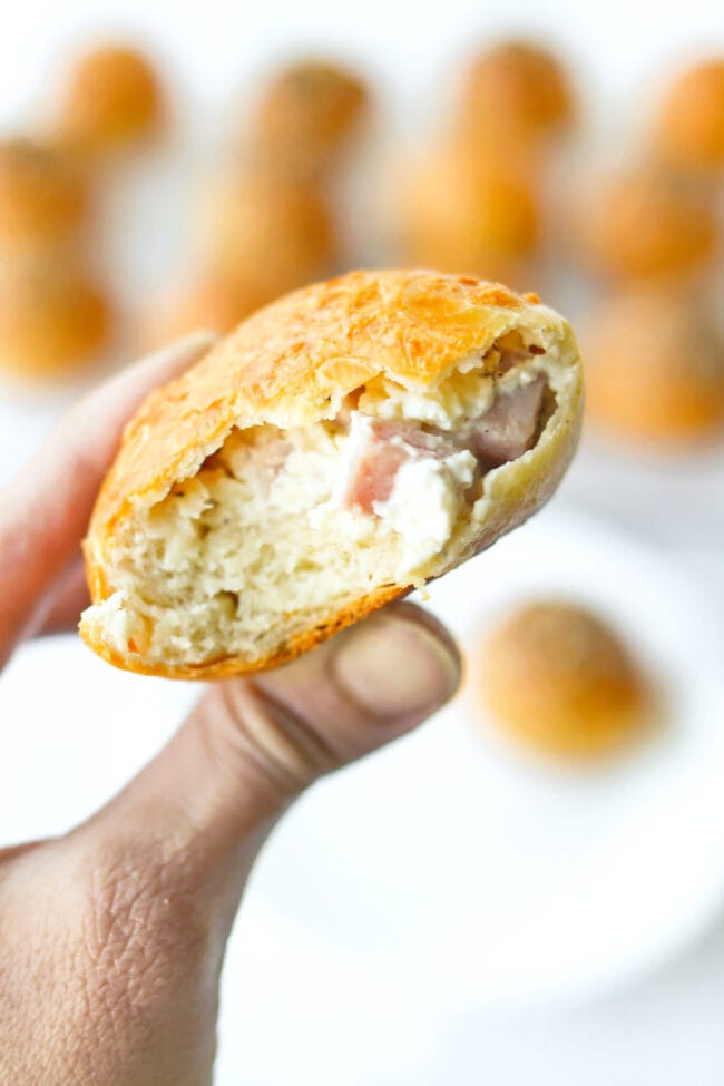 Hand holding up a ham and cream cheese stuffed bagel bomb with a bite taken out.