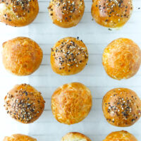 Top view of bagel bombs lined up on parchment paper. Text overlay "Greek Yogurt Dough Stuffed Bagel Bombs" and "thatspicychick.com".