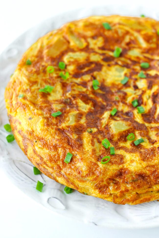 Close-up front side view of Spanish Omelette garnished with chopped spring onion on a plate.