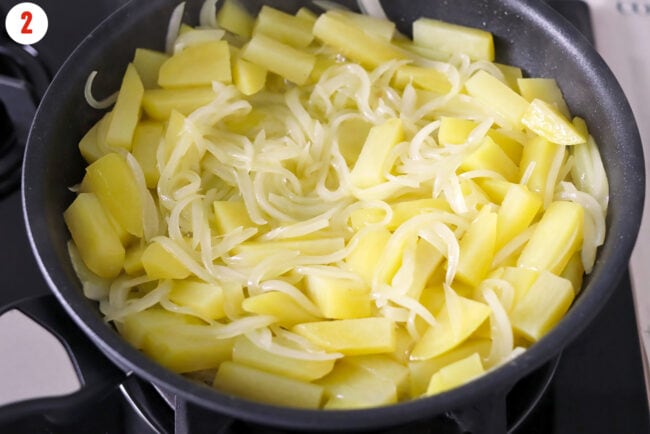 Potatoes and sliced onion cooking in a skillet on the stovetop.