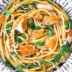 Close-up top view of salmon pasta with baby spinach and grated cheese in a plate.
