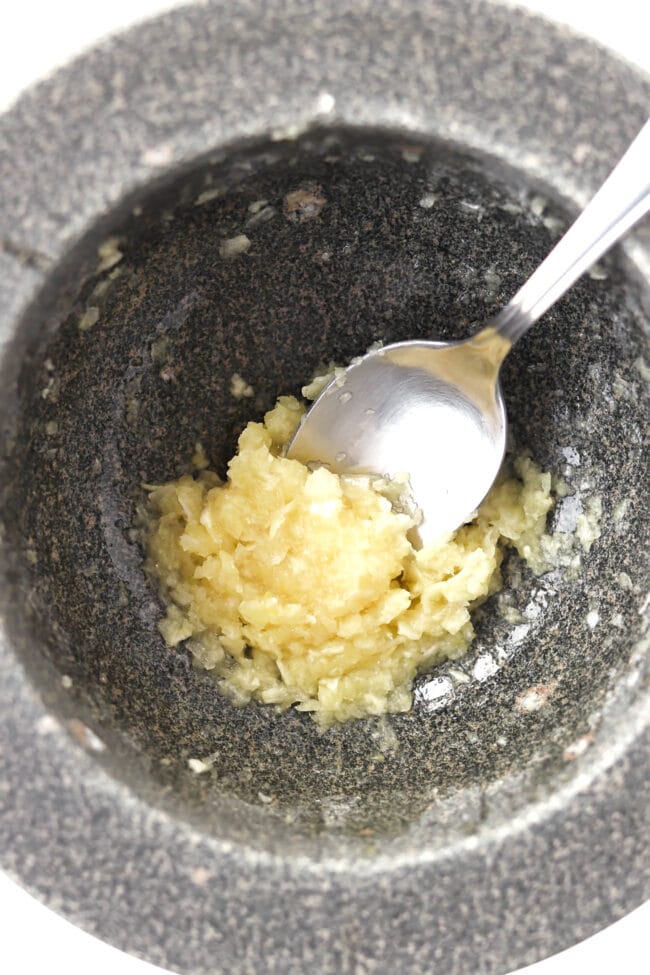 Smashed garlic in mortar with a spoon.