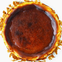 Top view of burnt cheesecake on a white background. Text overlay "Basque Burnt Cheesecake", "Lemon Flavored" and "thatspicychick.com".