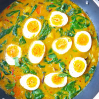 Top view of egg curry in a wok. Text overlay "Thai Yellow Curry with Eggs & Everyday Veggies!" and "thatspicychick.com".