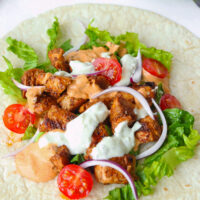 Chicken shish chunks on a tortilla with lettuce, sliced onion, cherry tomatoes, and sauces. Text overlay "Turkish Chicken Shish Kebab" and "thatspicychick.com".