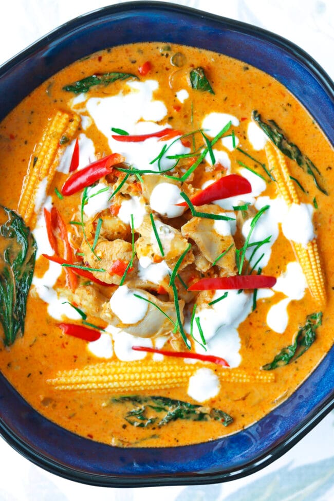 Close-up of bowl with panang chicken curry garnished with coconut cream, chilies, and kaffir lime leave strips.