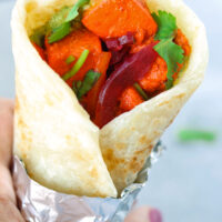 Hand holding up a paneer tikka kathi roll wrapped in foil.