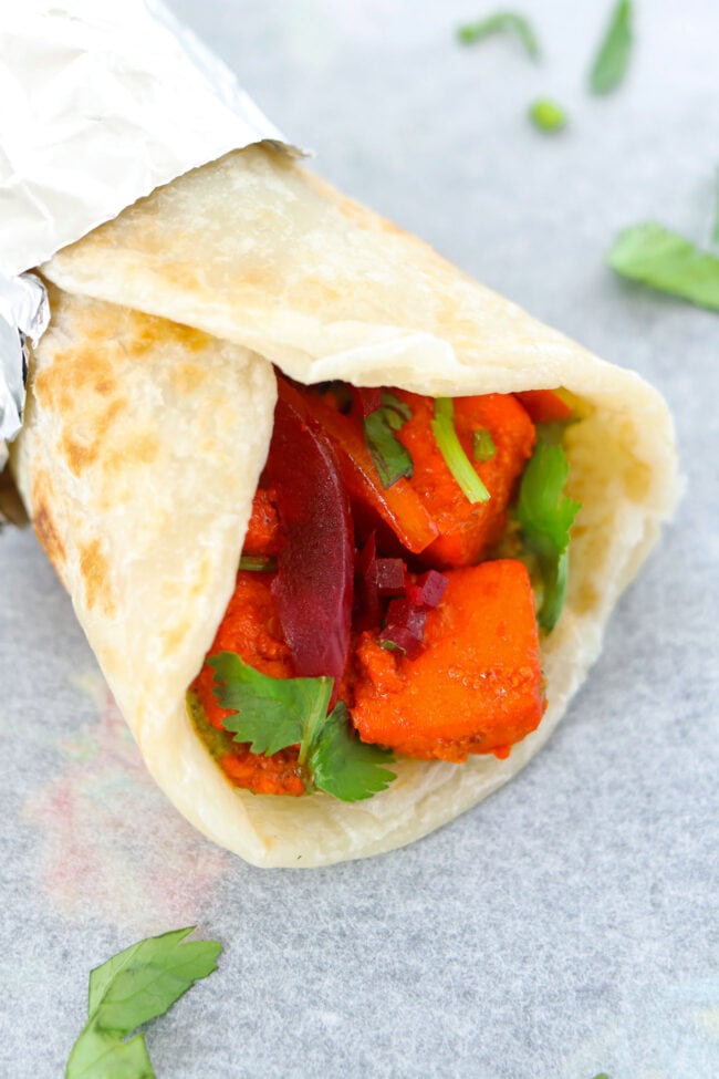 Close-up side view of a paneer tikka kathi roll with the back part wrapped in foil.