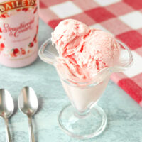 Ice cream scoops in an ice cream glass and two spoons on the side. Text overlay "Baileys Strawberries & Cream Ice Cream (No Churn!)" and "thatspicychick.com".