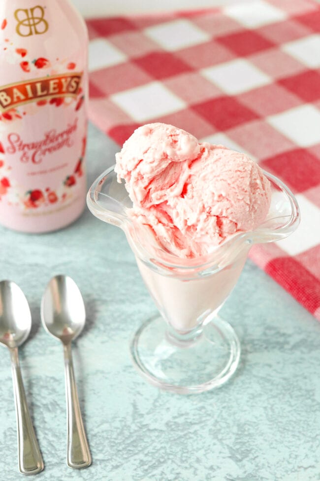 Strawberry ice cream in an ice cream glass, and Baileys Strawberries & Cream liqueur bottle behind.