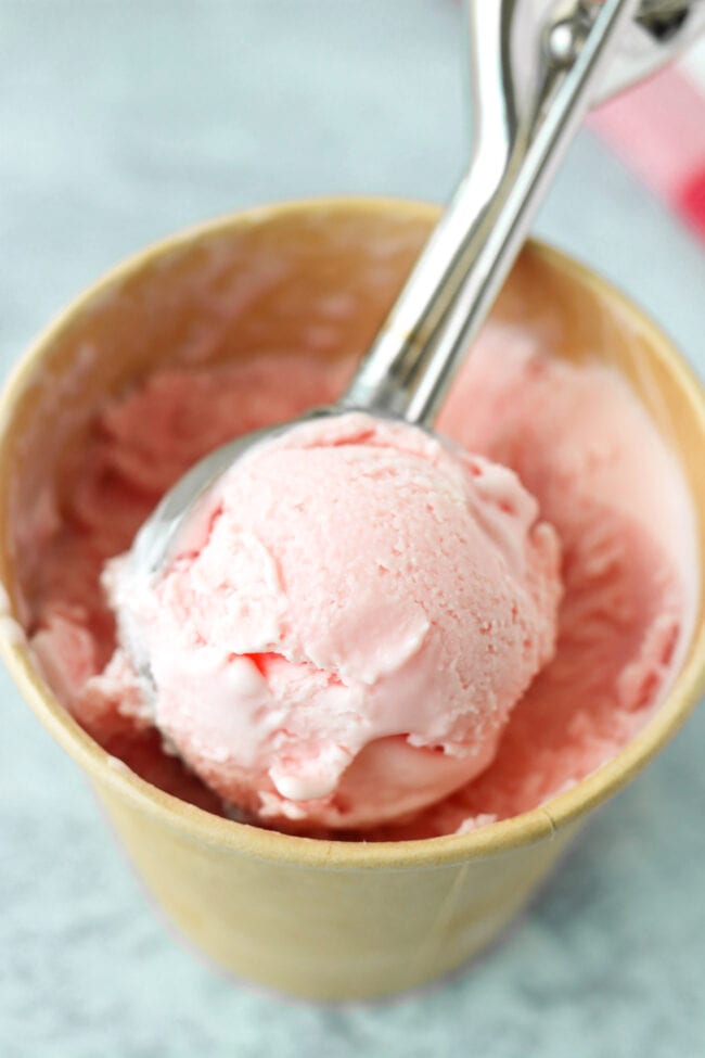 Ice cream scooper with a scoop of strawberries and cream ice cream in a pint carton.