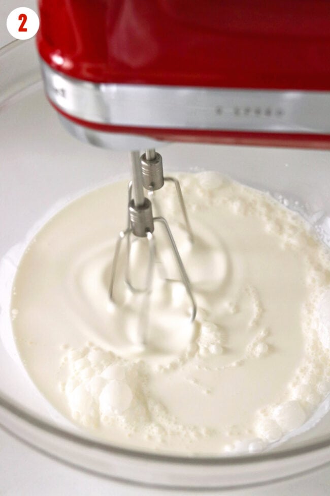 Electric hand mixer beating cream in a mixing bowl.