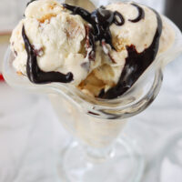 Ice cream scoops with hot fudge sauce in a dessert glass. Text overlay "No Churn S'mores Ice Cream" and "thatspicychick.com".