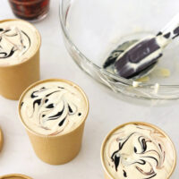 Assembling ice cream mixture in paper cartons. Text overlay "Baileys Espresso Crème Ice Cream (No Churn)", "With Hot Fudge Sauce Swirl!", and "thatspicychick.com".