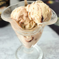 Ice cream in a tall dessert glass with a spoon. Text overlay "Baileys Espresso Crème Ice Cream (No Churn)", "With Hot Fudge Sauce Swirl!", and "thatspicychick.com".