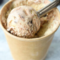 Front view of scooper with ice cream scoop in a paper carton. Text overlay "Baileys Espresso Crème Ice Cream (No Churn)", "With Hot Fudge Sauce Swirl!", and "thatspicychick.com".