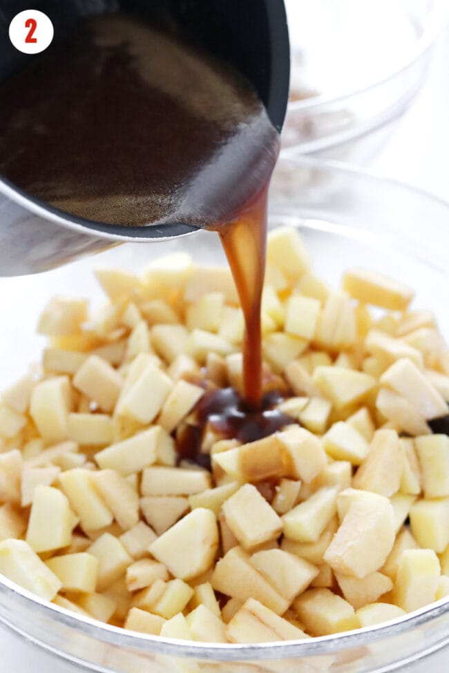 Pouring caramel sauce over diced apples in a large mixing bowl.