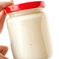 Hand holding up jar with dressing. Text overlay "The Best Easy Homemade Caesar Dressing" and "thatspicychick.com".