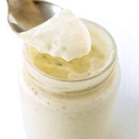 Spoon with dressing above jar. Text overlay "The Best Easy Homemade Caesar Salad Dressing" and "thatspicychick.com".