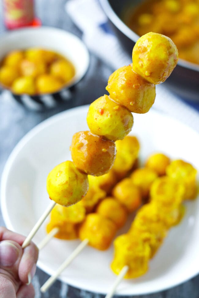 Hand holding up a wooden skewer with curry fish balls.