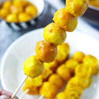 Hand holding up a wooden skewer with curry fish balls. Text overlay "Curry Fish Balls" and "thatspicychick.com".