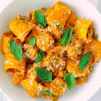 Top view of pasta in plate garnished with cheese and basil. Text overlay "Spicy Pumpkin Vodka Pasta with Juicy Italian Sausage" and "thatspicychick.com".