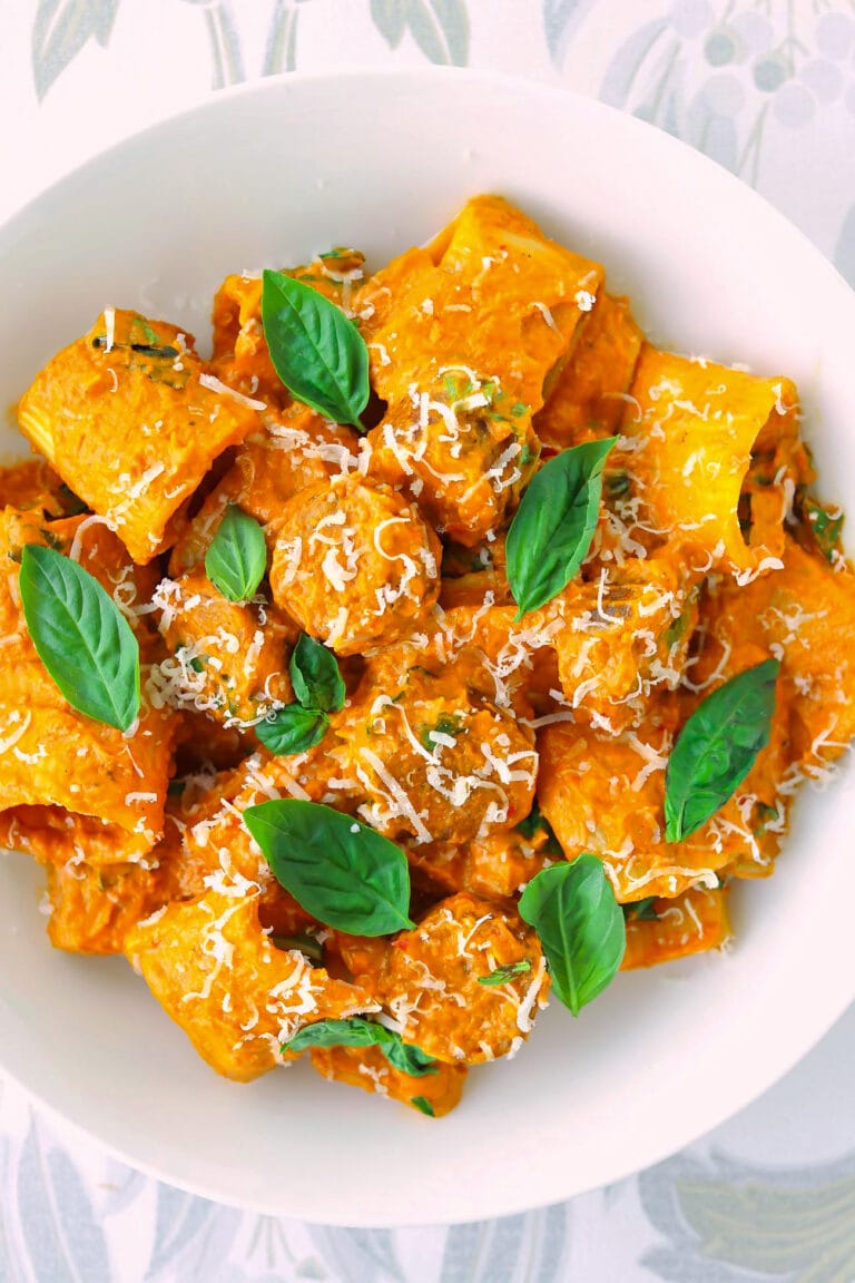 Plate with spicy pumpkin vodka pasta garnished with fresh basil leaves.