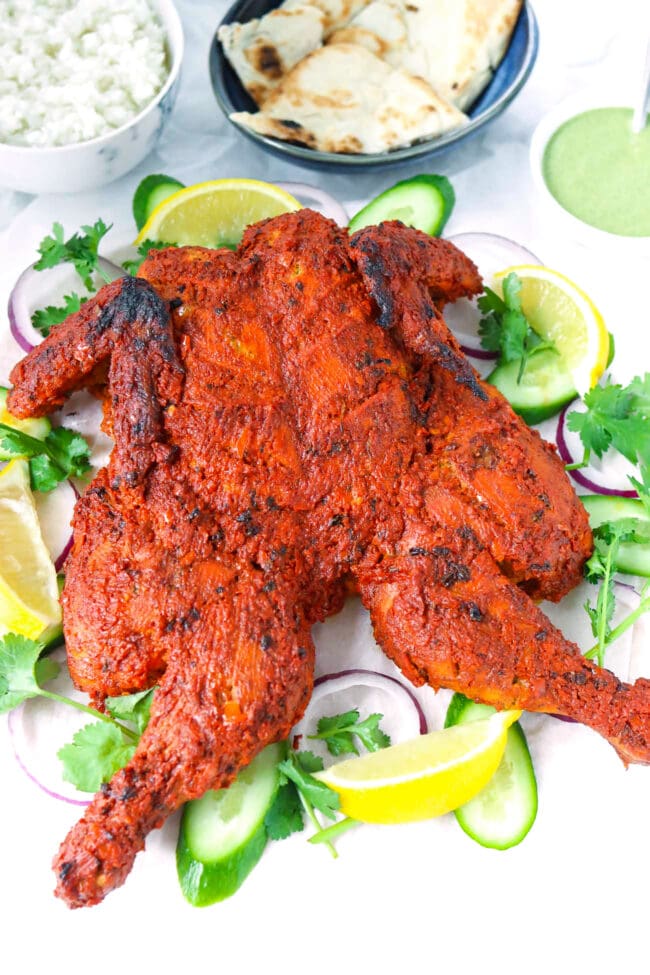 Front view of a spatchcocked Tandoori chicken on a serving platter.