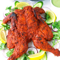 Front view of Tandoori chicken with garnishes on a serving platter. Text overlay "Whole Roasted Tandoori Chicken" and "thatspicychick.com"