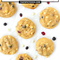 Top view of cookies on parchment paper. Text overlay "Dried Berries & White Chocolate Soft Muffin Cookies" and "thatspicychick.com".