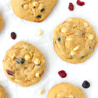 Close-up of soft muffin cookies surrounded with dried berries and white chocolate chips on parchment paper.
