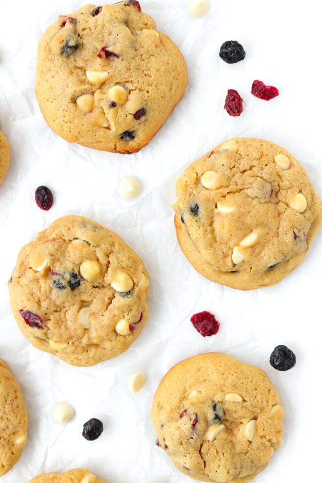 Close-up of soft muffin cookies surrounded with dried berries and white chocolate chips on parchment paper.