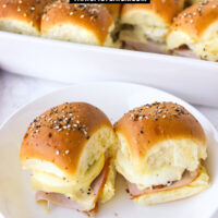 Two sliders on a plate and sliders in a baking dish behind. Text overlay "Ham Egg & Cheese Breakfast Sliders" and "thatspicychick.com".